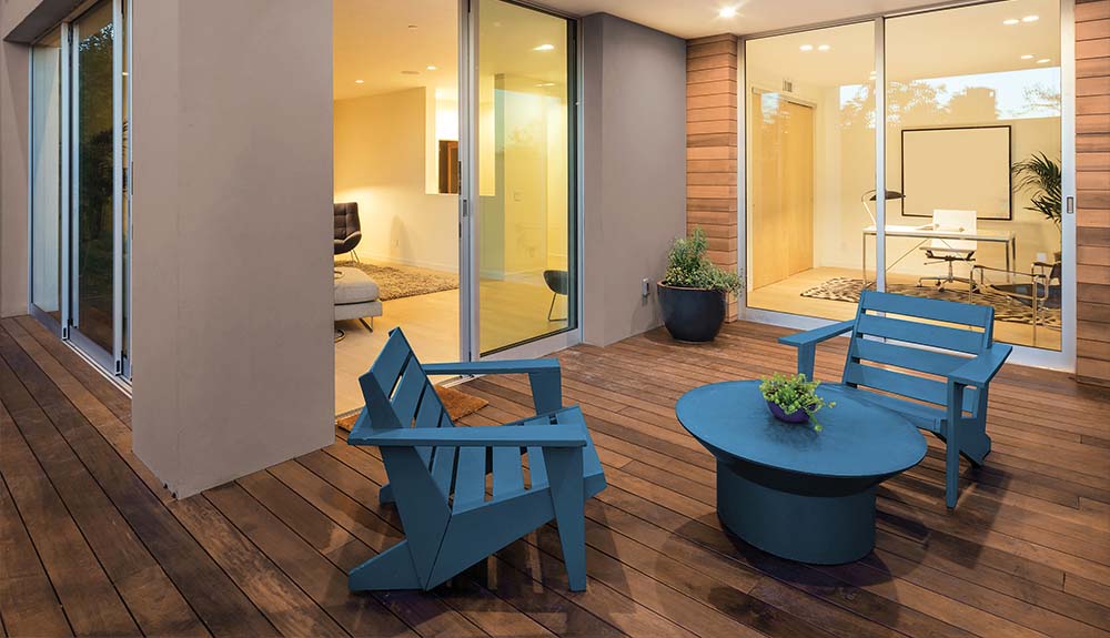 Two wooden patio short lounging chairs and a table all painted blue outside on the deck