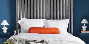 Bedroom with blue walls, white sheets, an orange accent pillow and two white lamps on the night stands on either side of the bed