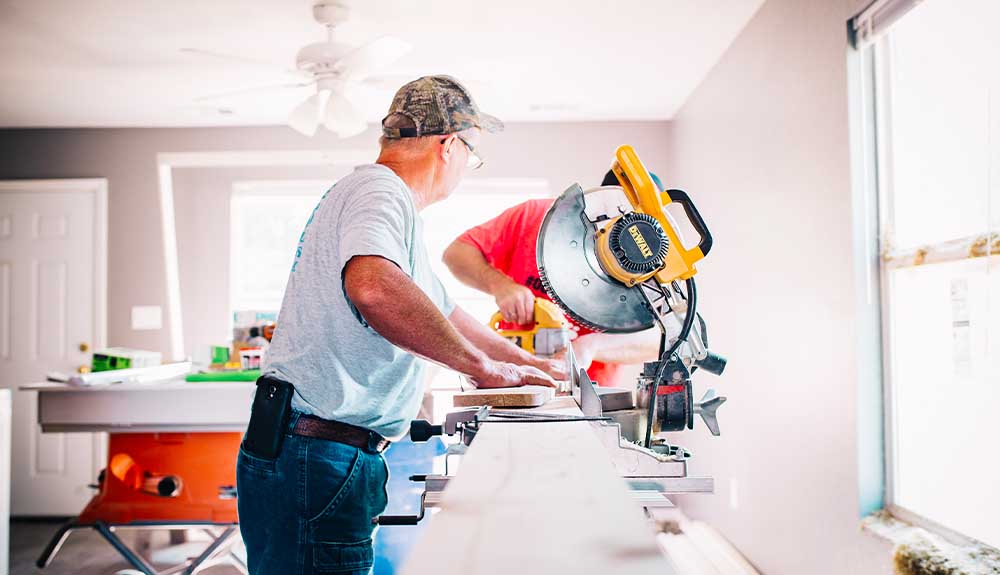 Two men are shown using a saw inside a home