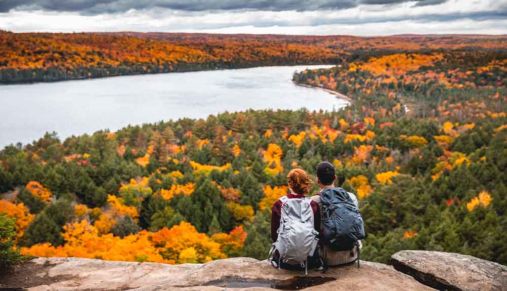 Two people are shown sitting on a rock overlooking a forest with a river running through it