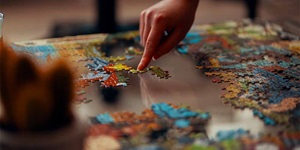 A finger is seen pushing pieces of a puzzle on a table