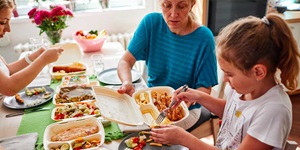 A family sits at the dinner table helping themselves to food from takeout containers