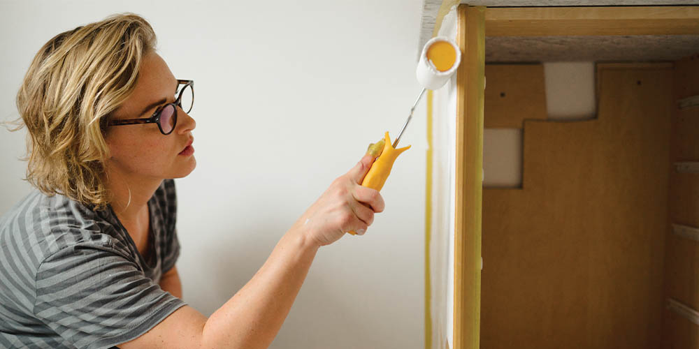 A woman paints the front of her kitchen cabinets