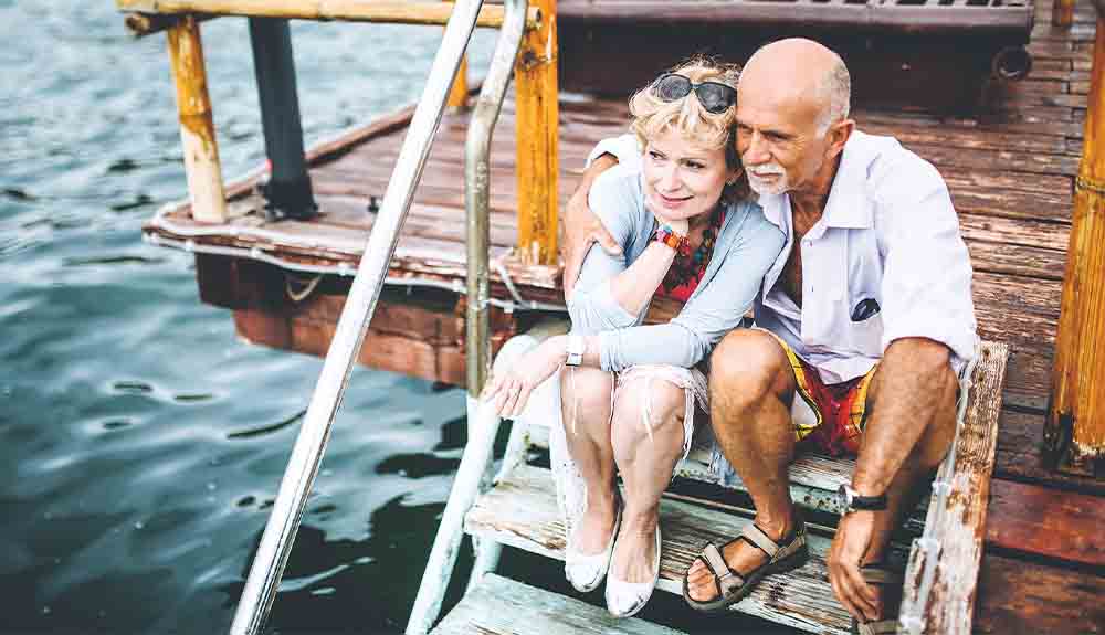 An older couple sit together on a dock