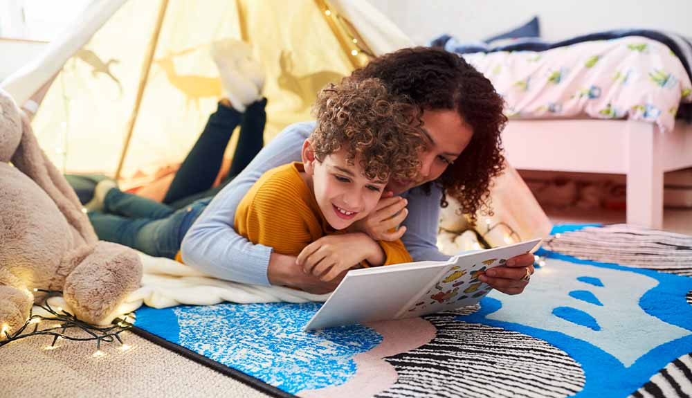 A parent and child are shown reading a book together in a tent set up in a bedroom