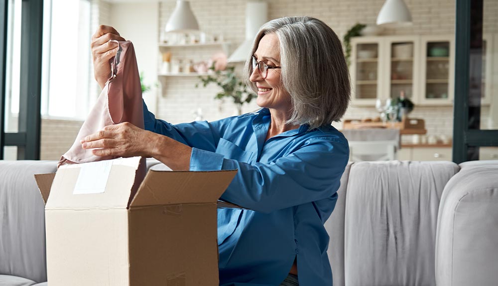 An older woman pulls a light pink clothing item out of a brown box