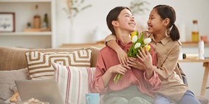 A mother holds a bouquet of white tulips while sitting on a couch with her daughter