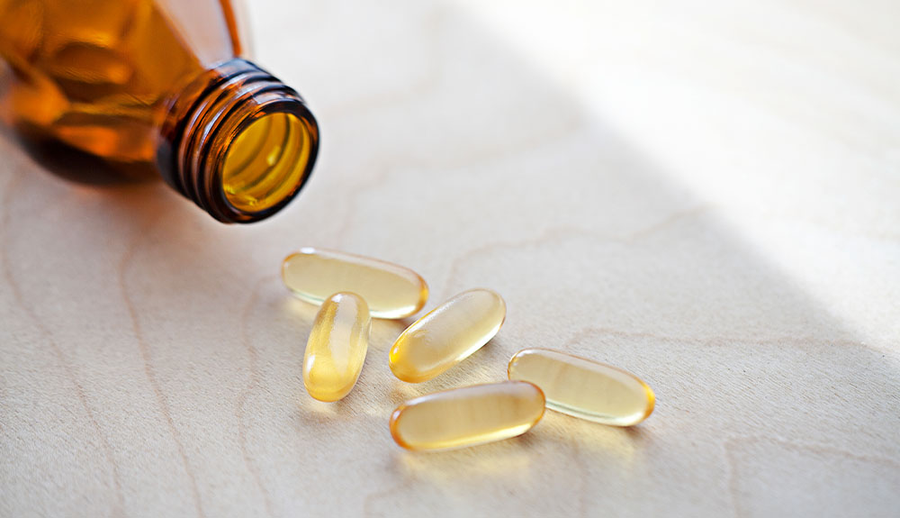 Yellow translucent pills are shown on a table with a brown bottle next to them