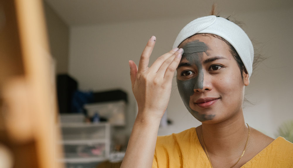 A woman spreads a grey paste on her face