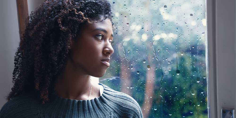 A woman looks out a window with rain drops splattered on it