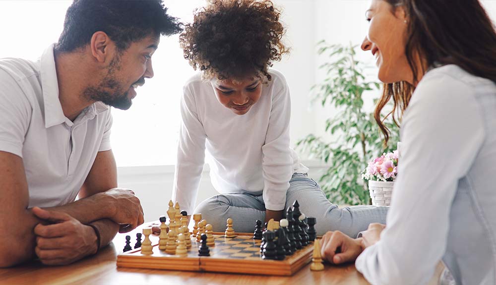 Two parents play chess while their child looks on