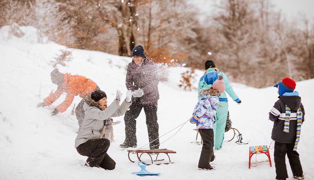 A family is shown playing in the snow, with sleds nearby