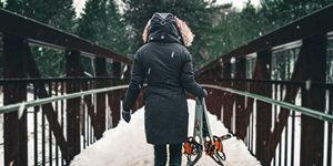 A person is shown from behind, carrying a pair of snowshoes while walking on a pedestrian bridge
