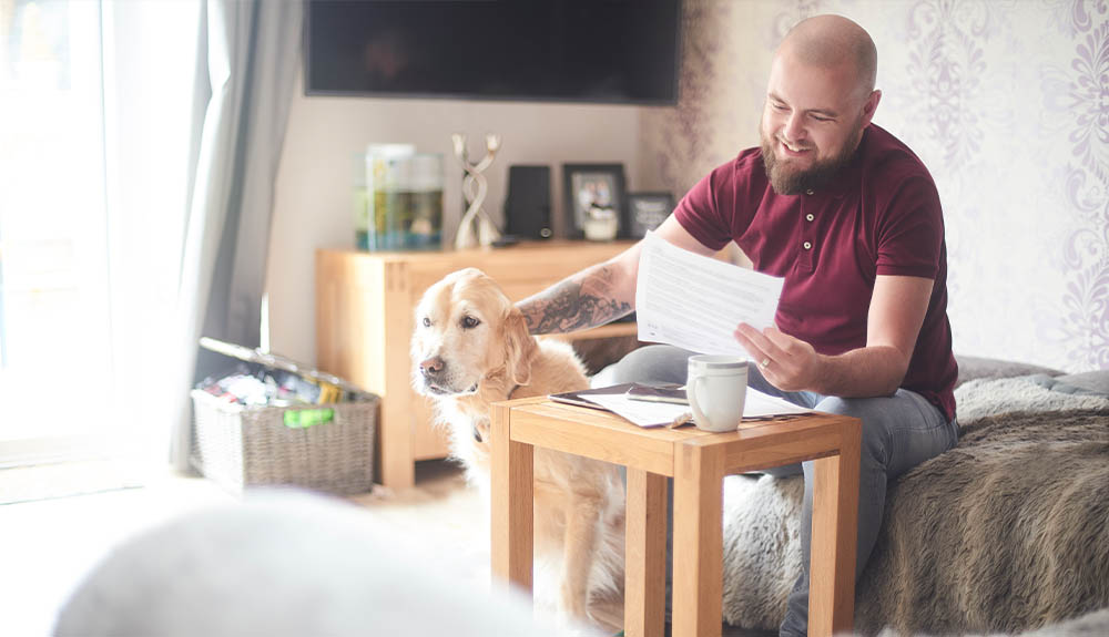 A man reads through some papers while petting his caramel-coloured dog