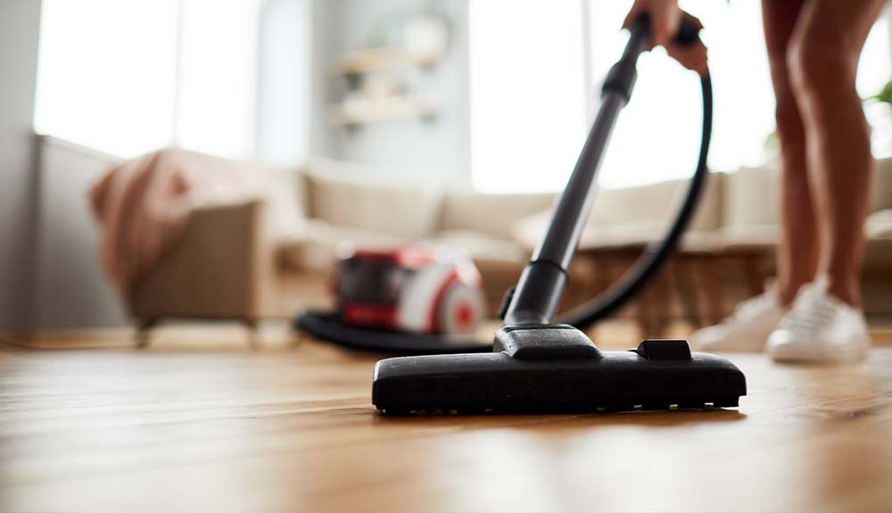 A vacuum is shown on a hardwood floor with a couch in the background