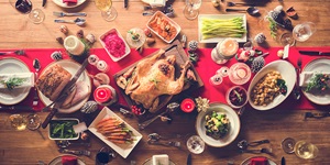 Overhead view of a roast turkey and dishes around it including roast carrots, asparagus, stuffing, Brussels sprouts, ham, sweet potatoes and cranberry sauce