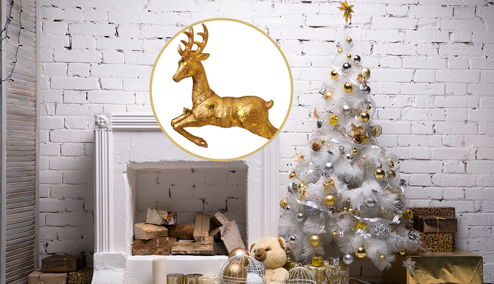 A white fireplace in a white painted brick room, a white Christmas tree with metallic holiday ornaments on it and a gold deer on top