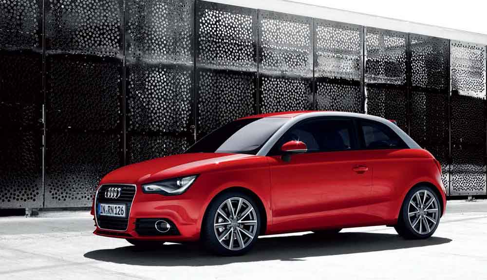 A red Audi A1 is shown parked in front of a black fence