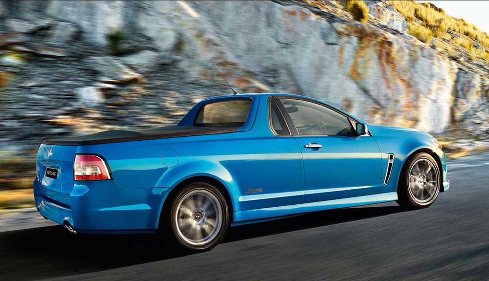 A blue Holden Ute is shown driving next to a rocky mountainside
