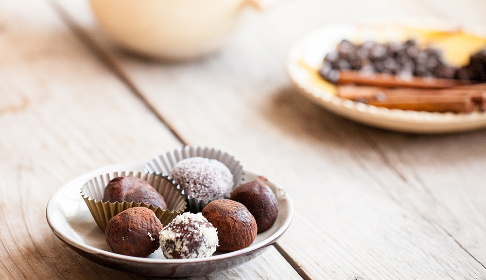 Close up shot of six chocolate truffles on a plate sitting on a wooden table