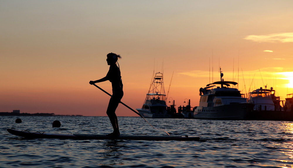 A person is seen on a standup paddle board on the water at sunset