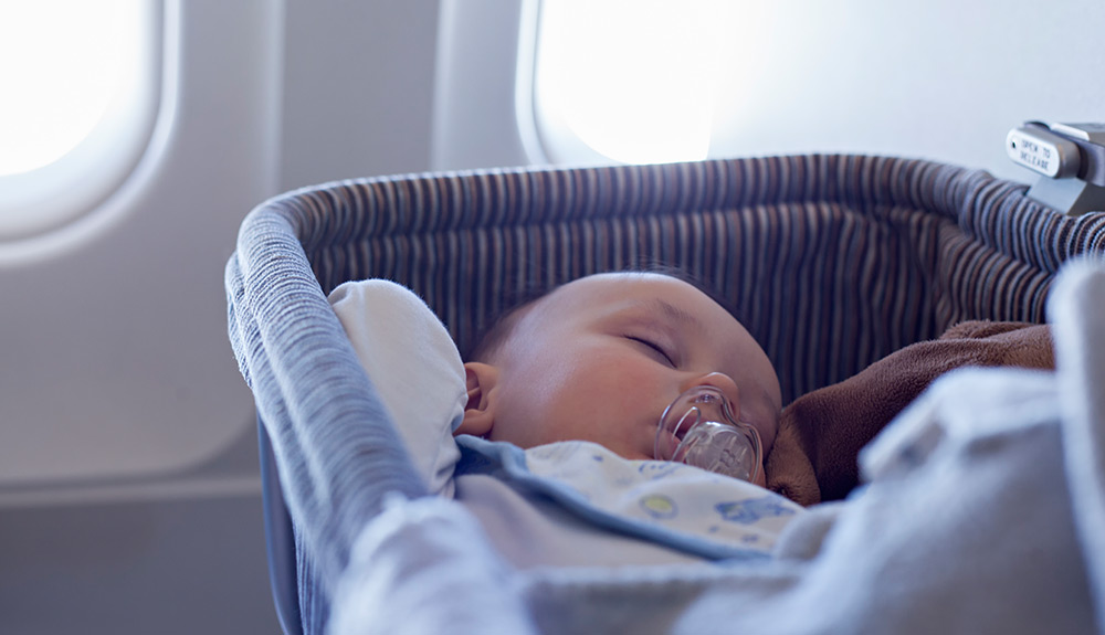 Baby wearing bib with soother in mouth sleeps quietly in soft padded carrier