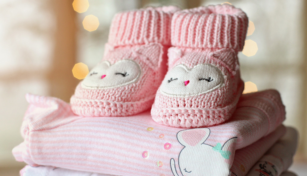 Neatly folded pink baby clothes stacked with knit pink booties on top