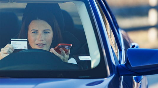 Woman in a car holding CAA membership card and calling roadside assistance.
