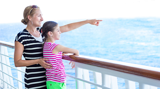 A mother points out across the horizon to her cute daughter. The two are enjoying a family cruise ship vacation together