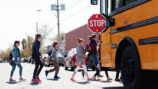 Group of elementary school kids getting in a yellow school bus at school's out. Boys and girls age 8-11. They seem happy to finish the school. 