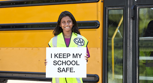 Safety school patroller holding a sign in front of the school bus