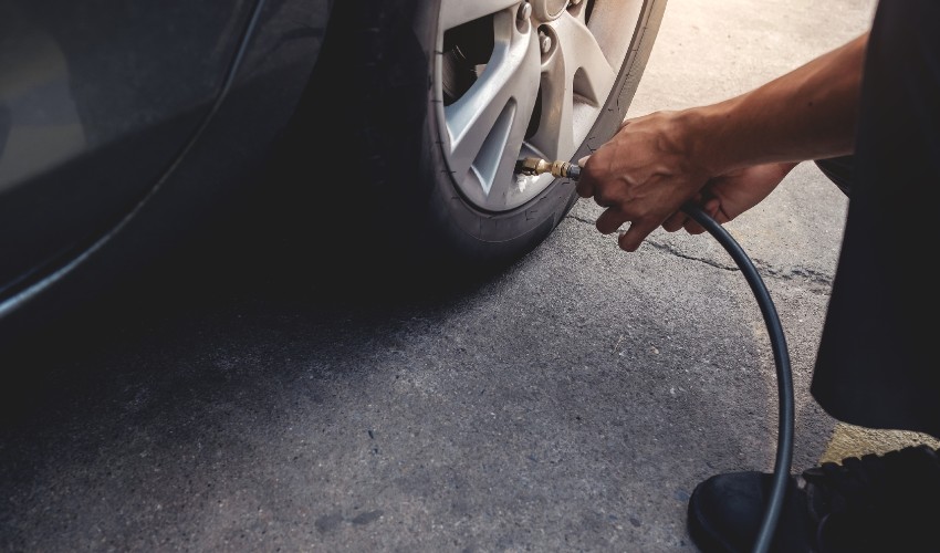 Man filling parked car tire with air.