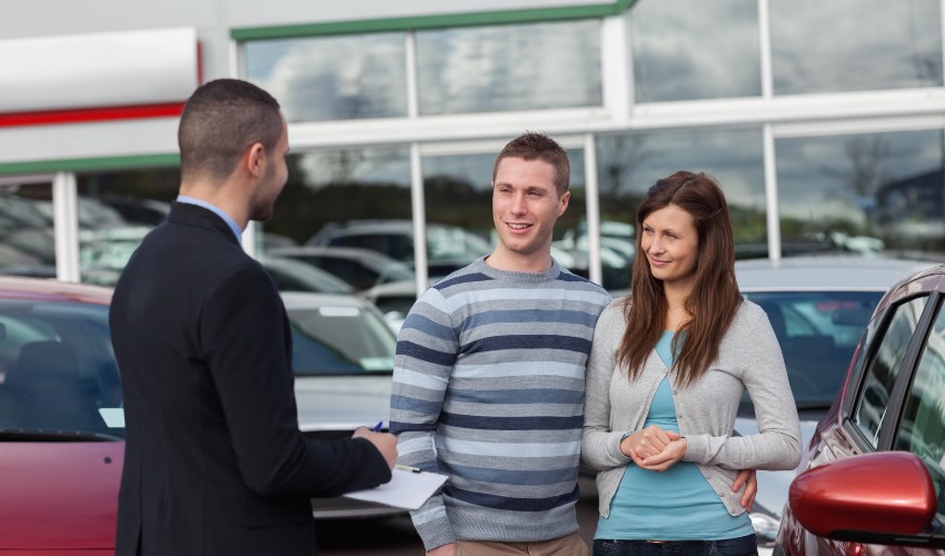 Car salesman talking to a couple at a dealership.