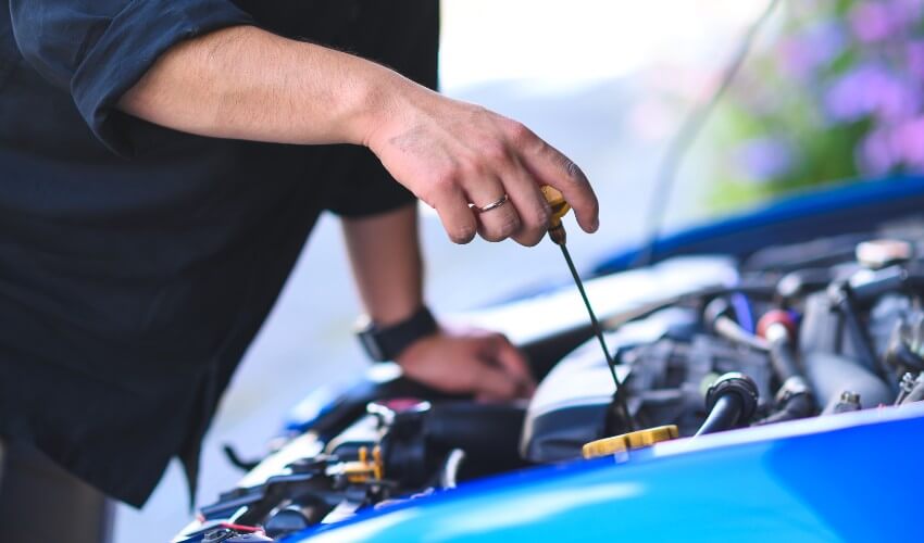 Close-up of hands of a mechanic checking car engine oil under the hood.