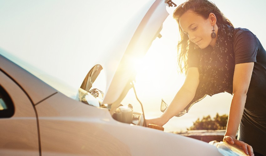 Woman looking under the hood of her car in summer.