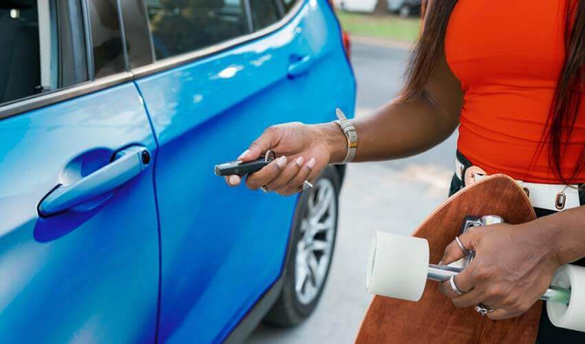 Woman holding skateboard using remote control key to lock car