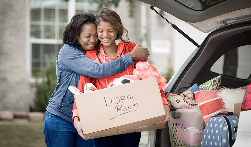 Mom hugging daughter at car packed for school.