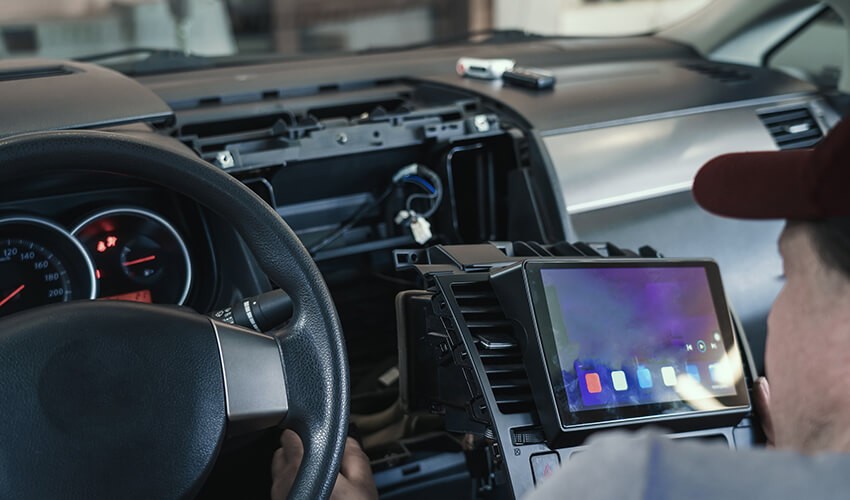 Auto electrician or repairman in car service installs multimedia sound system or car radio in auto dashboard panel.