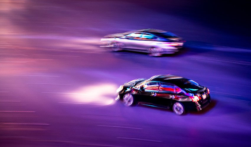 Two cars racing on a city street at night.