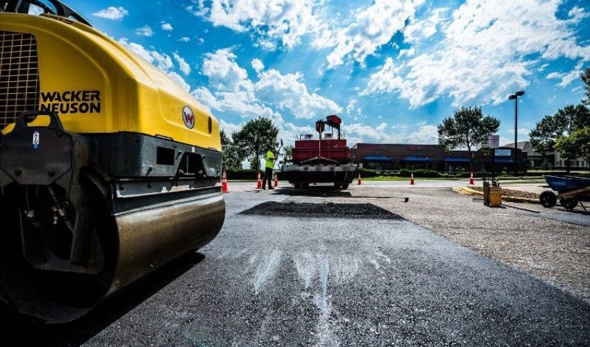 Construction workers distribute fresh asphalt on a road section and levels it for repair.