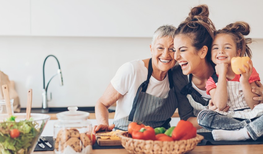 Grandmother, mother and young daughter at kitchen counter happily preparing a meal.