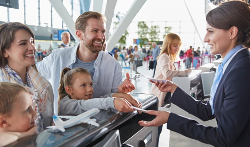 Family of four at airport getting tickets from agent.