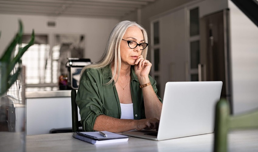 middle aged women seated at kitchen table working on laptop