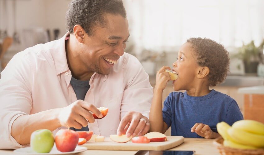 Father and son eating apples in the kitchen.