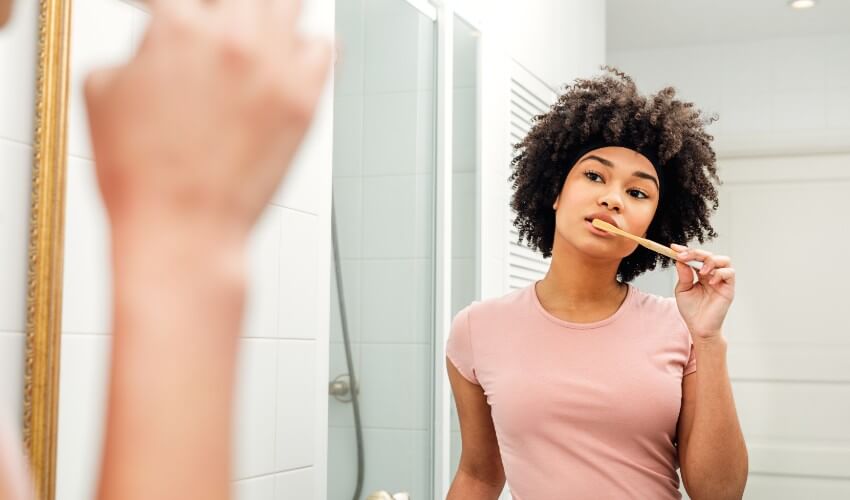 Woman brushing her teeth while looking in the mirror in the bathroom.