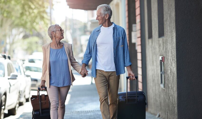 Mature couple walking on city street with suitcases.