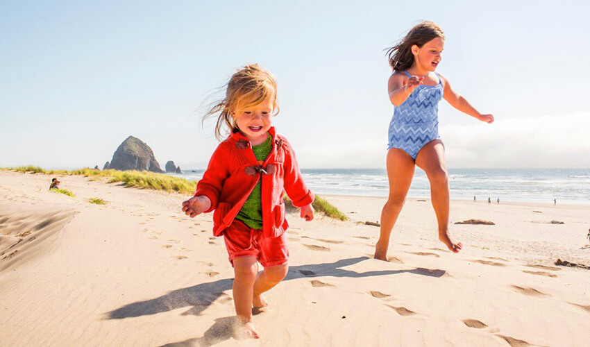 Two smiling small girls running around a sandy beach.