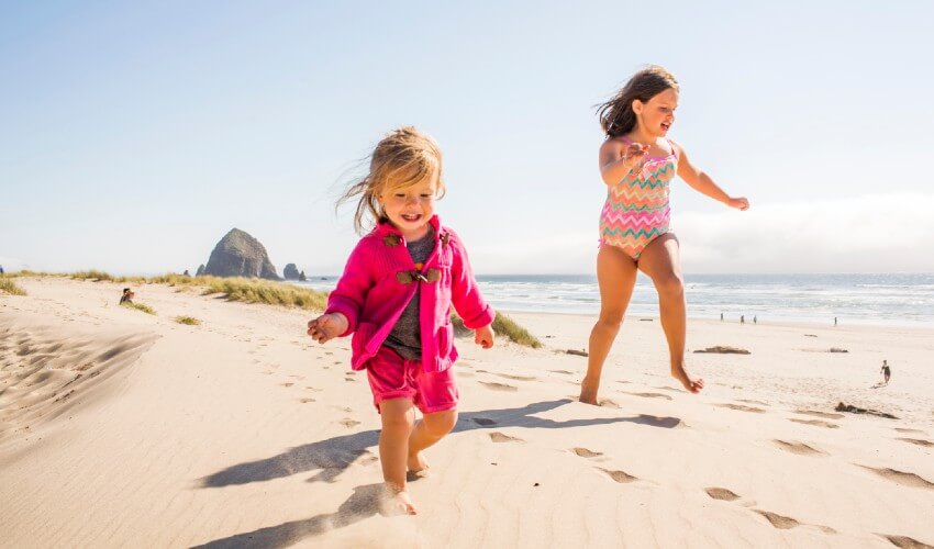 Two smiling small girls running on a sandy beach.