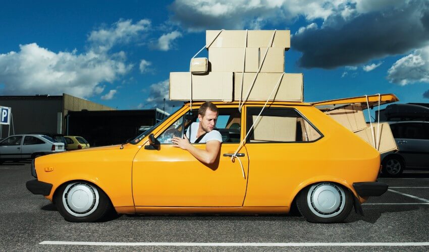 Man sitting in yellow car with boxes strapped on the roof.