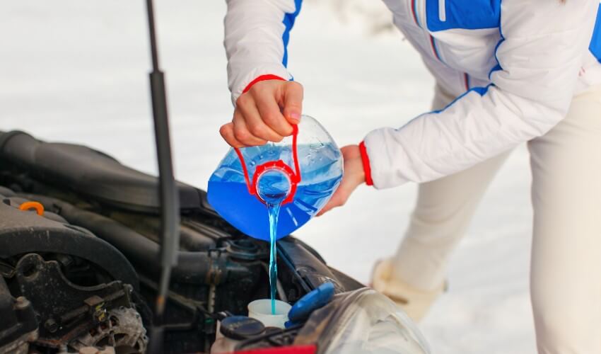 Woman in ski suit filling up windshield fluid.